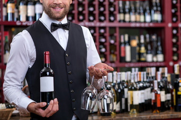 Cheerful young waiter is carrying alcohol drink in cellar