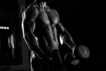 Strong man - bodybuilder with dumbbells in a gym, exercising wit