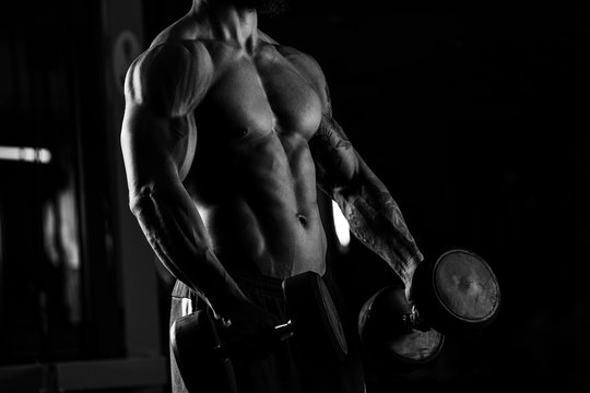 Strong man - bodybuilder with dumbbells in a gym, exercising wit