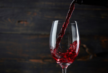 Fototapeta na wymiar Pouring red wine into the glass against dark wooden background
