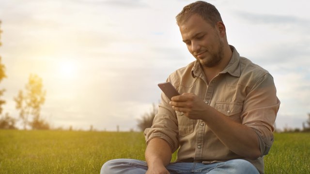  Handsome young man talking on smart phone at sunset outdoors. Using smartphone for a phone call, smiling happy wearing urban hipster outfit outdoors in peaceful autumn nature