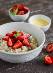 oatmeal with strawberries and honey in white bowl on dark wooden surface