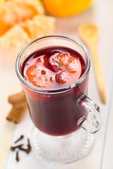 Hot spiced mulled red  wine with mandarin segments on top, with cloves, cinnamon sticks, mandarin and wooden spoon (Selective Focus, Focus one third into the mandarin segments on the drink)