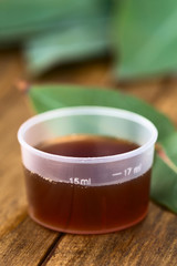 Eucalyptus cough syrup in medicine cup with fresh Eucalyptus leaves (Selective Focus, Focus on the 15ml sign on the cup)