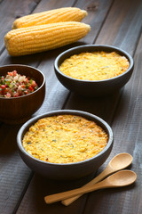Traditional Chilean corn pie Pastel de Choclo with Pebre sauce in the back, photographed with natural light (Selective Focus, Focus in the middle of the dish)