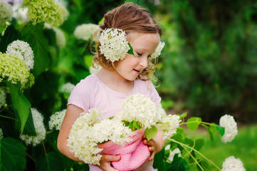 cute happy child girl playing with hydrangea flowers in summer garden