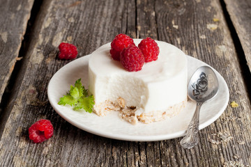 cheesecake with fresh raspberries and mint leaves on top on a wo