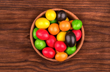A pile of multicolored candy peanuts in chocolate in a bowl on the table top view