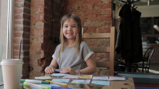 Smiling little girl draws with markers at a table in a coffee