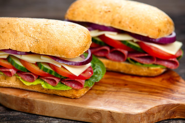 Sandwich with lettuce, slices of fresh tomatoes, cucumber, red onion, salami and cheese