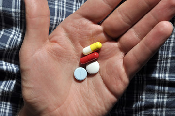 Close up of four white, red, blue and yellow tablets on hand
