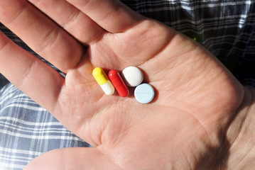 Close up of four white, red, blue and yellow tablets on hand