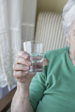 
wrinkled hand of a senior person holding a glass of water