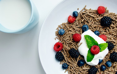 Muesli with berries in white dish on blank white table with blue