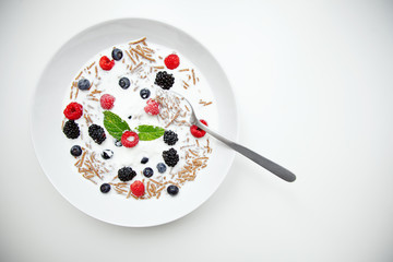 Muesli with milk and berries for breakfast in white dish with sil