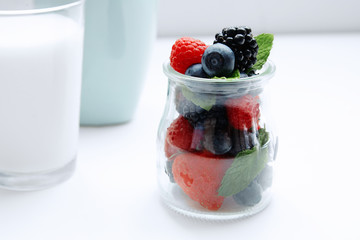 Close up berries and mint in jar and glass of milk