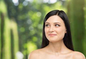 A portrait of a smiling brunette lady who is looking at something on the right side. Tropical landscape in blur on the background.