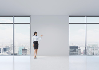 Full length brunette girl in a formal clothes is pointing out something by her hand on the white wall. A modern panoramic office in Manhattan, New York.