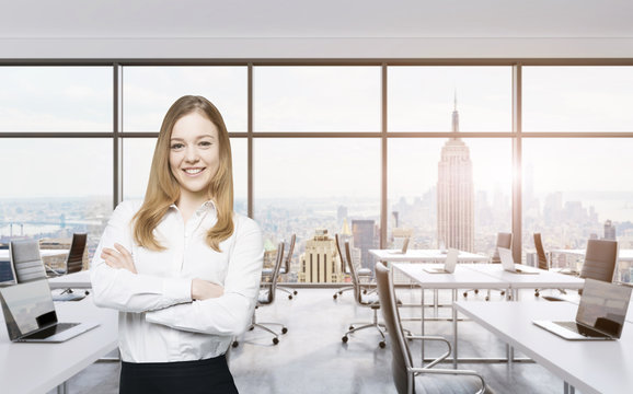 Smiling beautiful business lady with cross hands is standing in a modern panoramic office in New York City. Manhattan sunset view. Toned image.