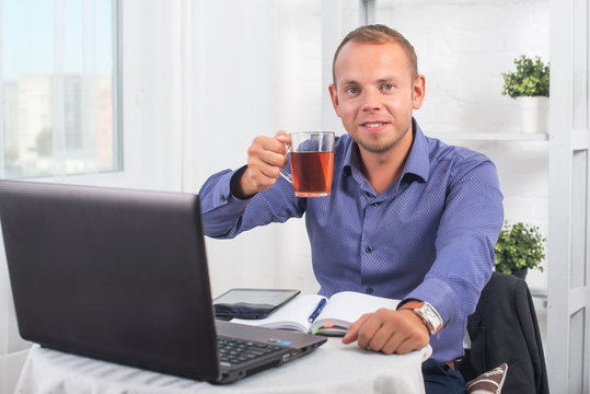 Businessman working in office, sitting at a table holding cup and looking straight