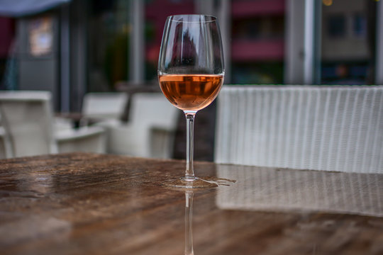 Close-up of a glass of rose wine on the brown table. Photographed on a rainy day. The table is wet.