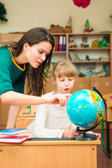 Fototapeta premium Teacher and pupil in the classroom looking at a globe