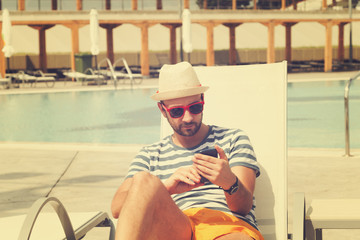 Young man on the swimming pool with cellphone.