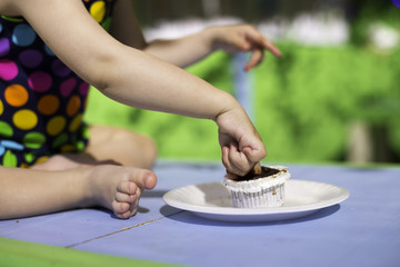 Fototapeta na wymiar Renkli puantiyeli mayo giymiş küçük bebek çikolatalı keki parmakları ile yemeye çalışıyor.