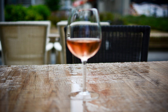 Glass of rose wine on the brown table. Photographed on a rainy day. The table is wet and focus is behind glass on purpose.