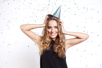 Young woman in a celebratory cap fooling around at a party on the background of falling confetti