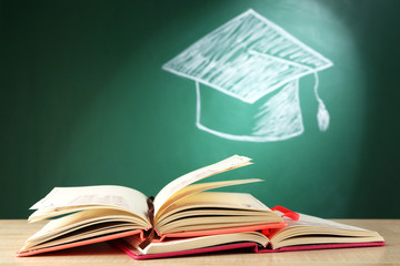 Open books and bachelor hat drawing on blackboard background