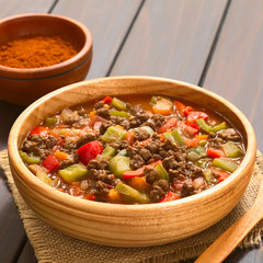 Vegan goulash made of soy meat (textured vegetable protein), capsicum, tomato and onion, served in wooden bowl, photographed with natural light (Selective Focus, Focus one third into dish)