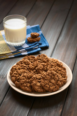 Chocolate oatmeal cookies on plate with a glass of milk in the back, photographed with natural light (Selective Focus, Focus on the first cookies)
