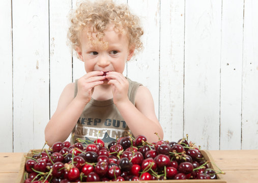 A Young Blond Curly Boy Eating Cherries