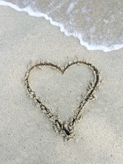 loving heart shape written in sand on beach with wave