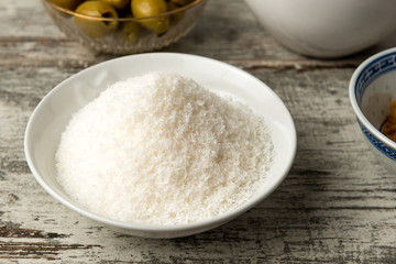 Cocco grattugiato e disidratato in una coppetta di ceramica bianca su un tavolo di legno