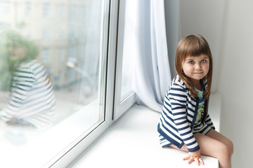 Fototapeta na wymiar Portrait of a little girl sitting on a windowsill