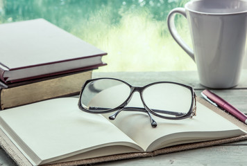 Fototapeta premium eyeglasses on open notebook with book,pen and coffee cup 