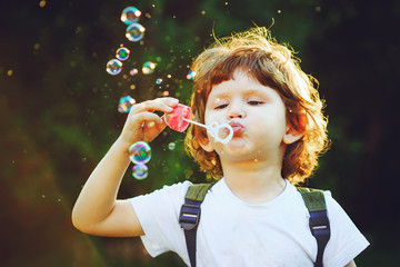 Child blowing soap bubbles in summer park.