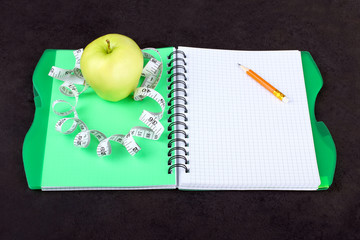 Notepad with measuring tape and Apple on a black background