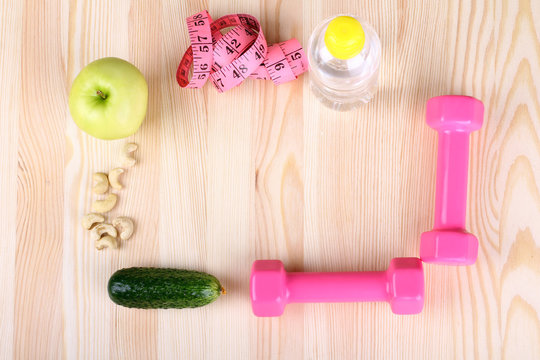 Apple,cucumber, measuring tape, wheel weights and water in bottle on wooden background