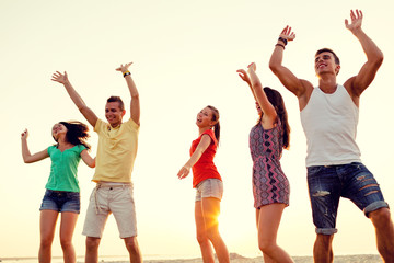 smiling friends dancing on summer beach