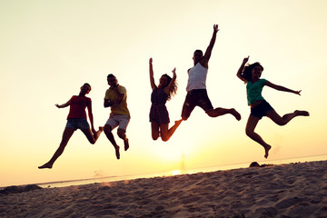 smiling friends dancing and jumping on beach