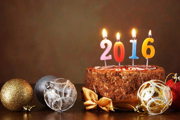 New Year 2016 still life. Chocolate cake and decorative tree balls with burning candles on brown...