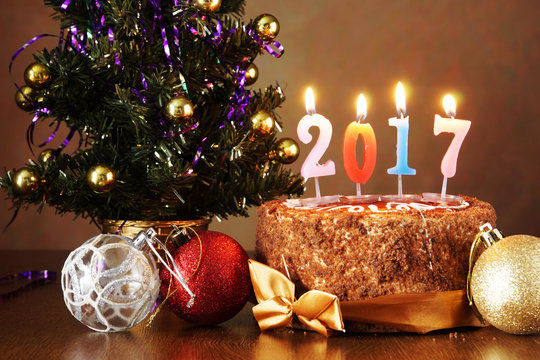New Year 2017 still life. Chocolate cake and artificial fir tree with burning candles on brown background