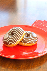 two donuts with sweet zebra coloring on a red plate on a wooden dining table. top view.