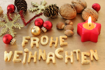 Frohe Weihnachten in Schrift mit Weihnachtskerze, Weihnachtskugeln, Haseln&uuml;sse, Waln&uuml;sse, Tannenzapfen und Eiskristall