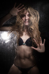The girl in black lingerie for a wet glass on a black background.