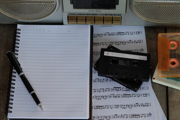 concept song composer: old tape cassette, song notes, cassette, notebook and pen on wooden...