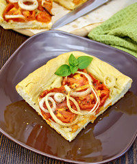 Pie with onions and tomatoes in brown plate on board